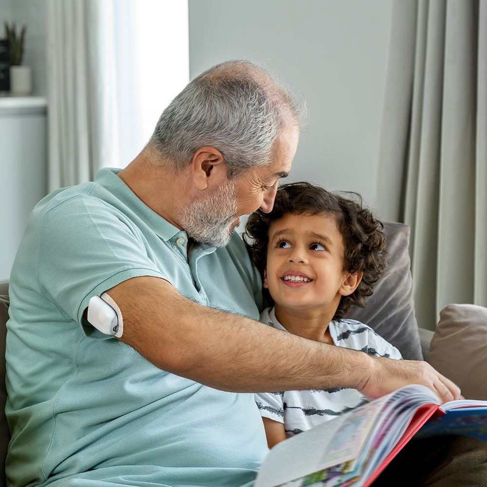 Grandfather wearing an Omnipod pod reading with his grandson – healthcare brand campaign Dubai